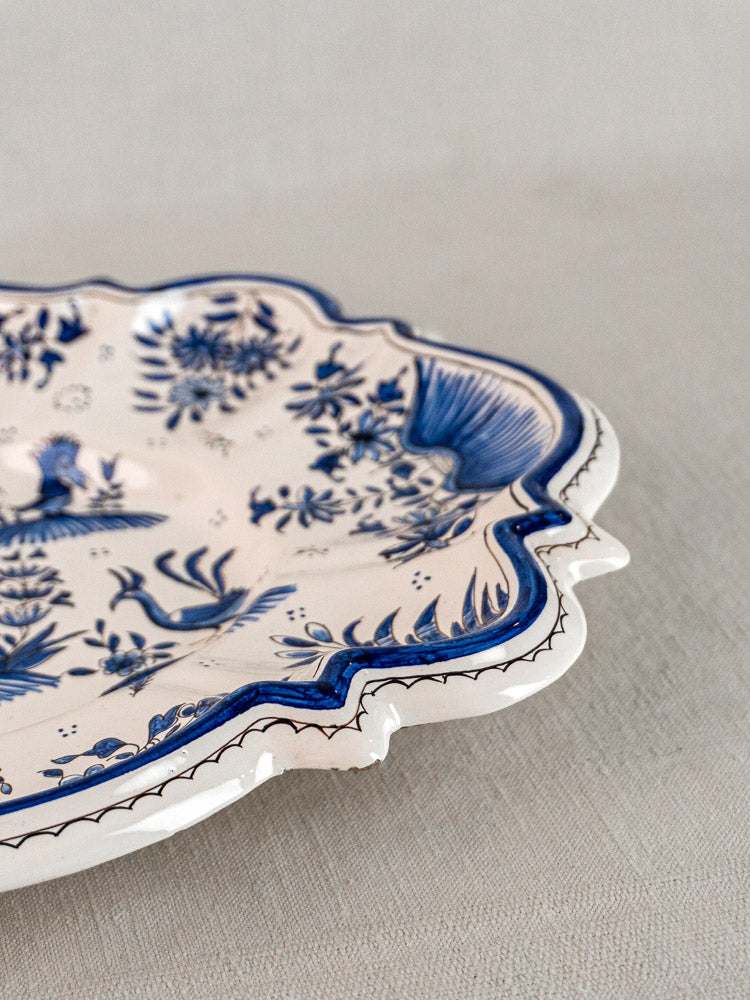 Antique French faience platter with blue Moustiers floral and bird motifs on cream, on neutral fabric.