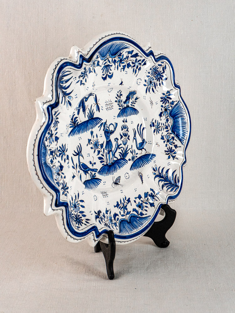 19th-century French Moustiers faience platter with scalloped edges and blue grotesque floral motifs, on black stand.