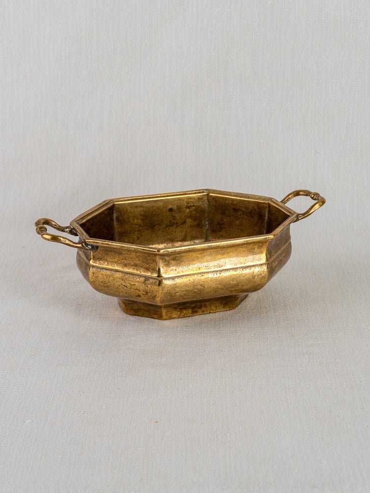 Small antique French octagonal brass bowl with two ornate handles on a light background.