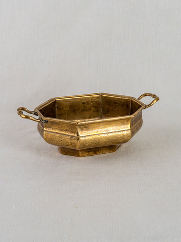 Small antique French octagonal brass bowl with two ornate handles on a light background.