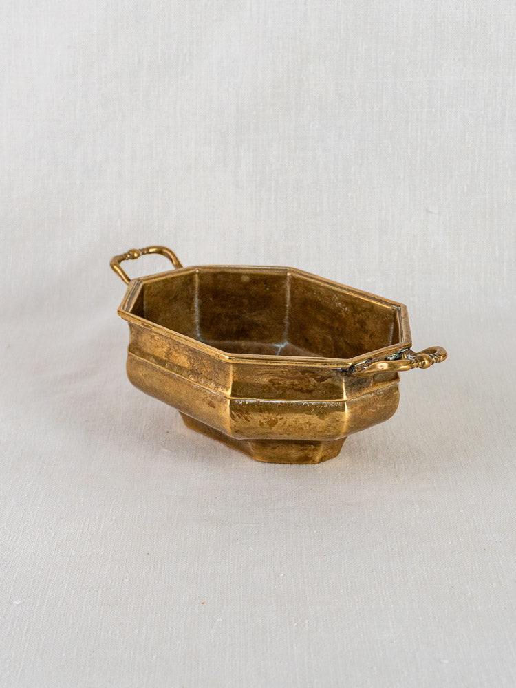 French octagonal brass coupe with two ornate handles on a light textured surface.