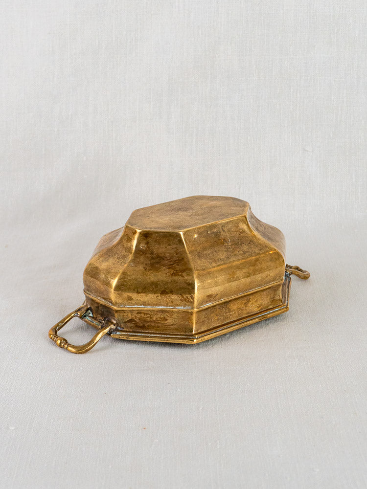 Small vintage French octagonal brass coupe with ornate handles and hinged lid on fabric background.