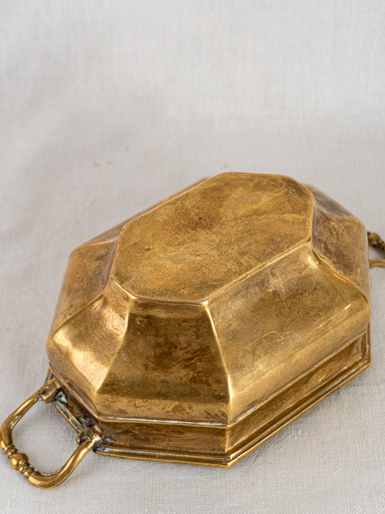 Antique French octagonal brass coupe with faceted lid and ornate handles on a light textured surface.