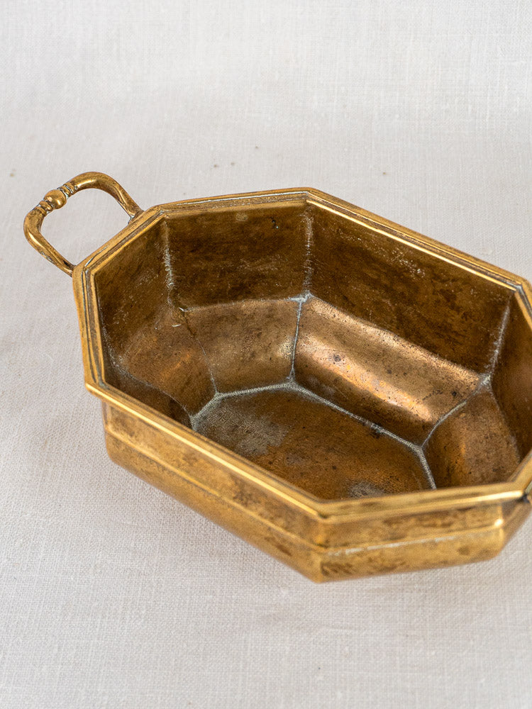 Antique French octagonal brass coupe with two handles and aged patina on light fabric background.