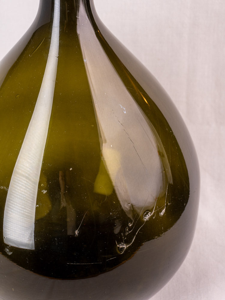 Antique French olive green hand-blown glass demijohn with applied neck ring and visible vintage imperfections.