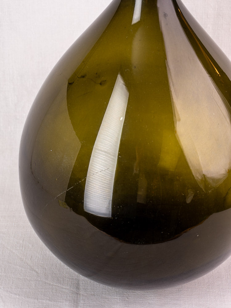 Rounded base of antique French olive green hand-blown glass demijohn, applied neck ring, on white background.