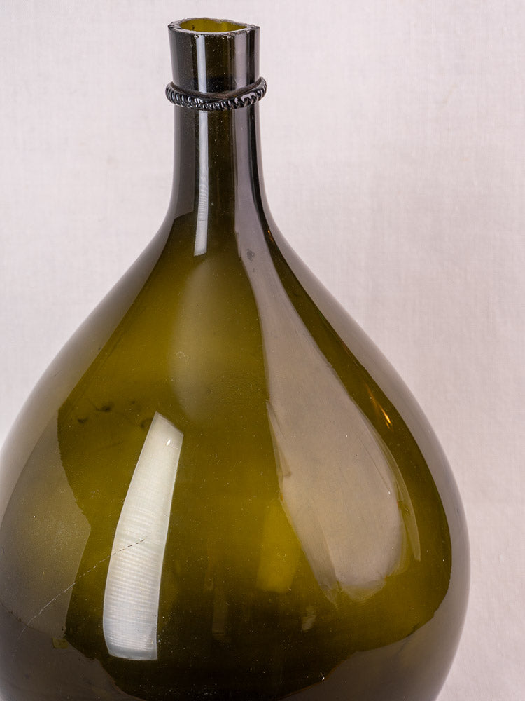 Antique French demijohn in olive green hand-blown glass with applied neck ring and rounded body on a light background.