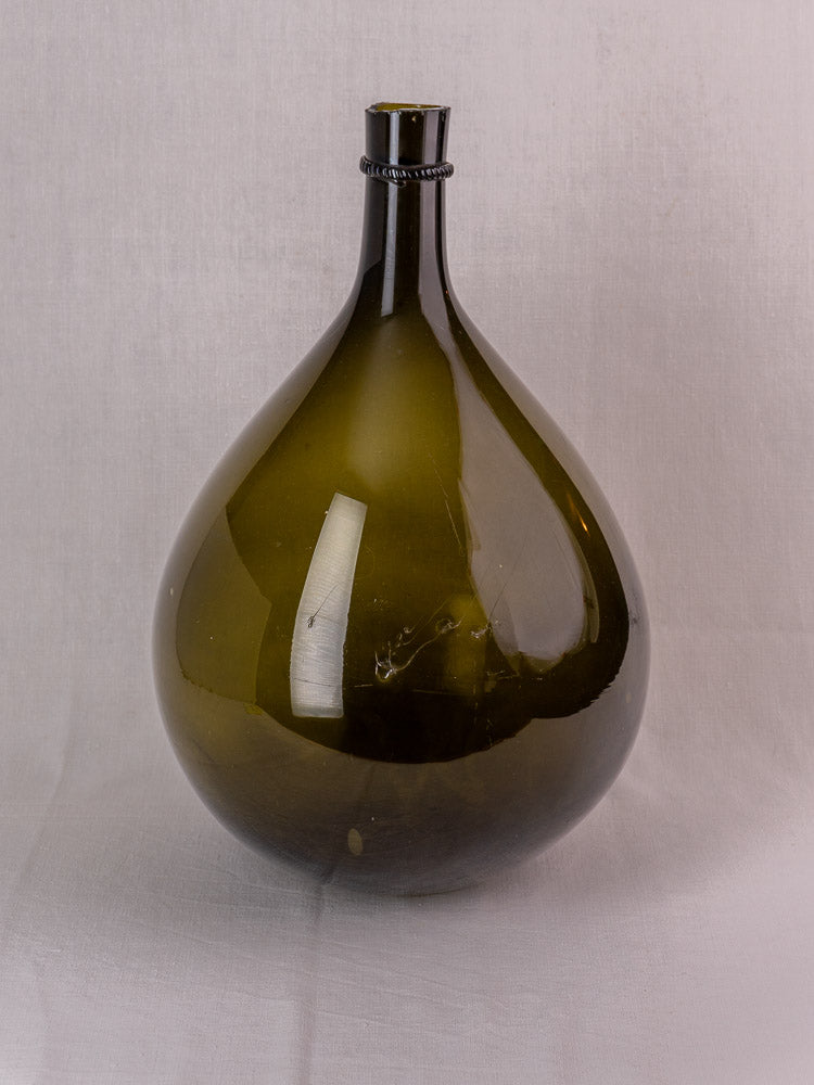 Antique French olive green hand-blown glass demijohn with applied neck ring on white cloth.