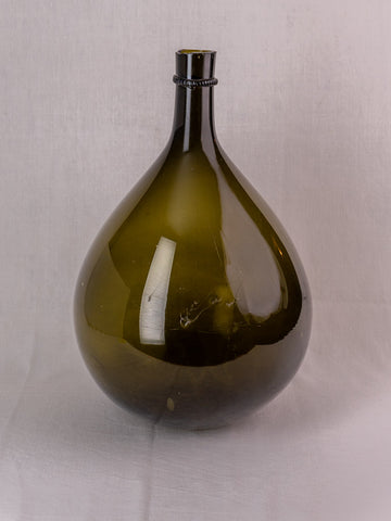 Antique French olive green hand-blown glass demijohn with applied neck ring on white cloth.