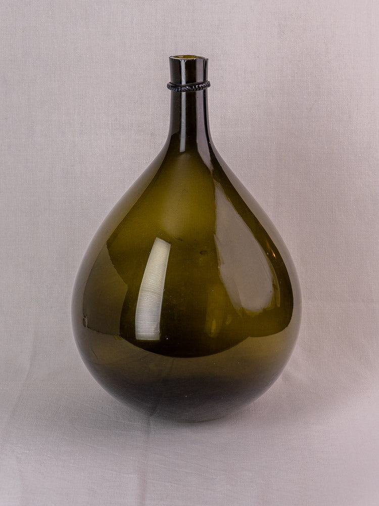 Antique French olive green hand-blown glass demijohn with applied neck ring on a light textured surface.