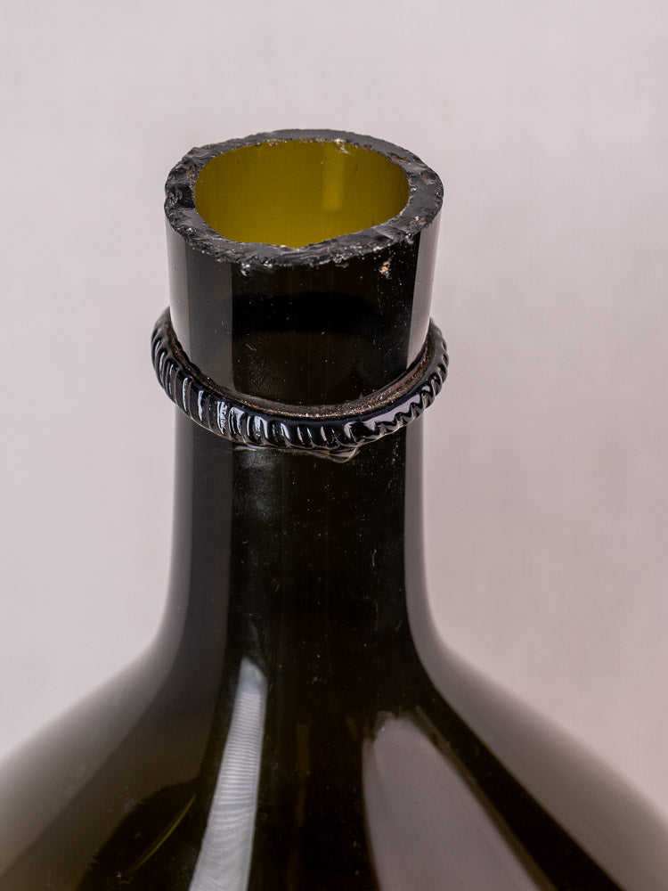 Antique French demijohn in olive green hand-blown glass with jagged rim and textured neck ring on plain background.