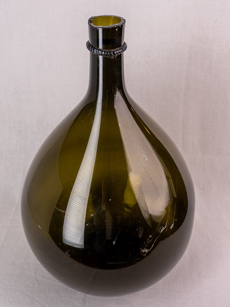 Antique French demijohn in olive green hand-blown glass, bulbous base and narrow neck, on a light background.