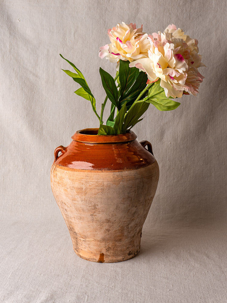 Antique French olive oil jar in glazed terracotta, brown and beige, with side handles, on gray background.