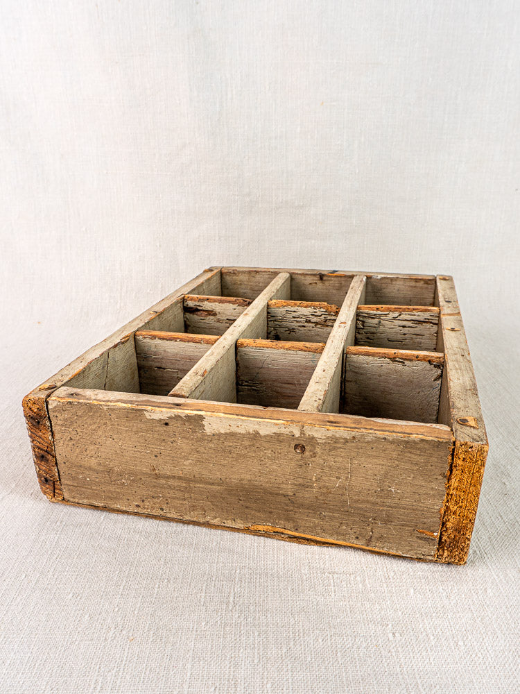 Antique French painted pine casier with nine compartments, showcasing rustic texture on light fabric surface.