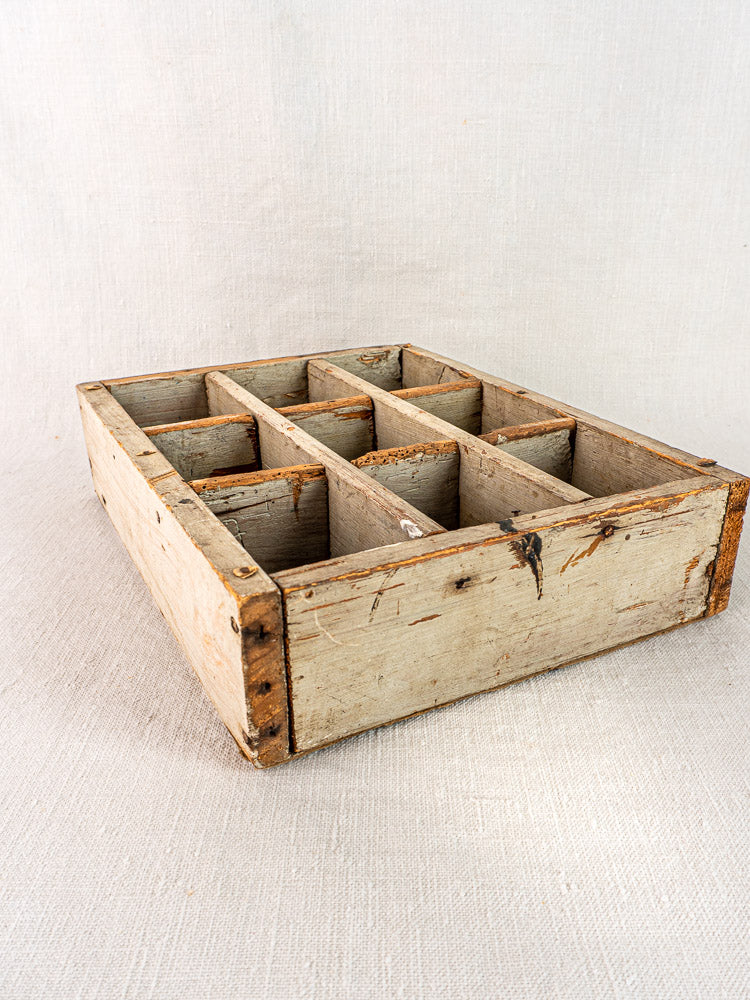 Antique French painted pine casier with nine compartments and aged patina, atop a light fabric surface.