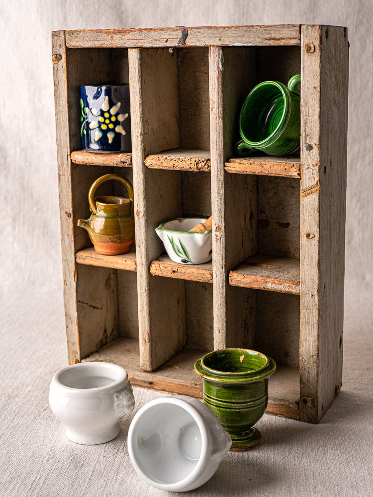 Antique French painted pine casier with 9 compartments displaying assorted ceramic cups and pitchers.