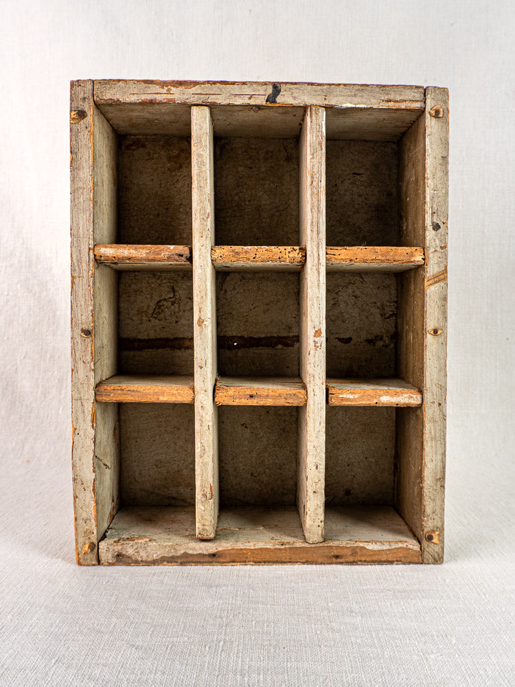 Antique French painted pine casier with nine compartments, worn paint, and visible wood grain on light fabric.