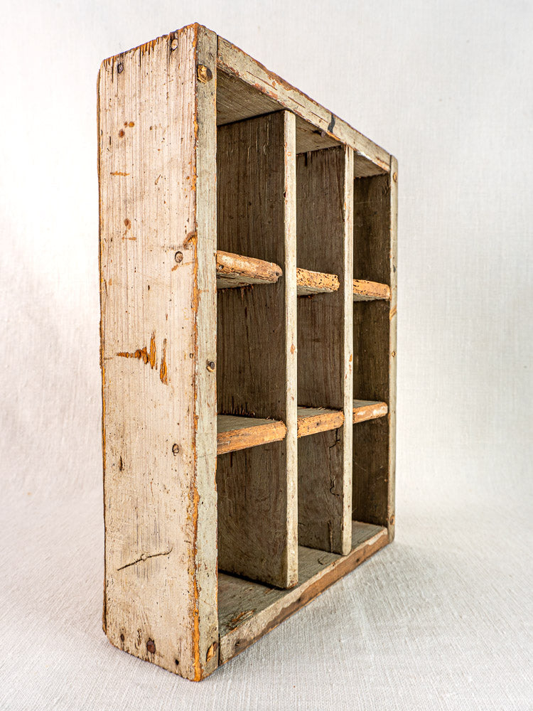 Antique French painted pine casier with nine compartments, worn edges, faded paint on light fabric surface.