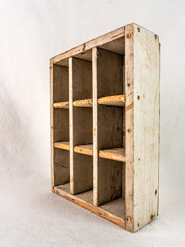 Antique French painted pine casier with nine compartments, showing aged wood, on neutral fabric.