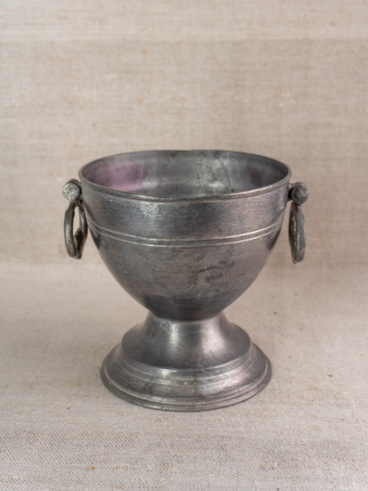 Antique French mid-19th century pewter footed bowl with side handles on textured beige fabric background.