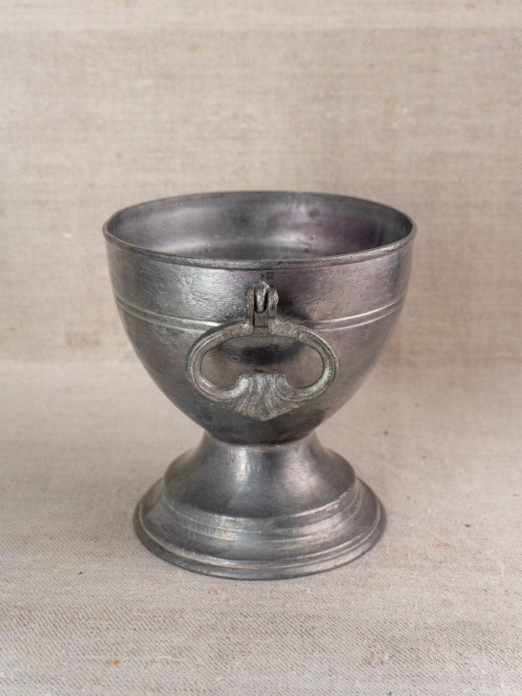 Antique French pewter footed bowl, mid-19th century, with wide bowl and ring handle on neutral fabric background.