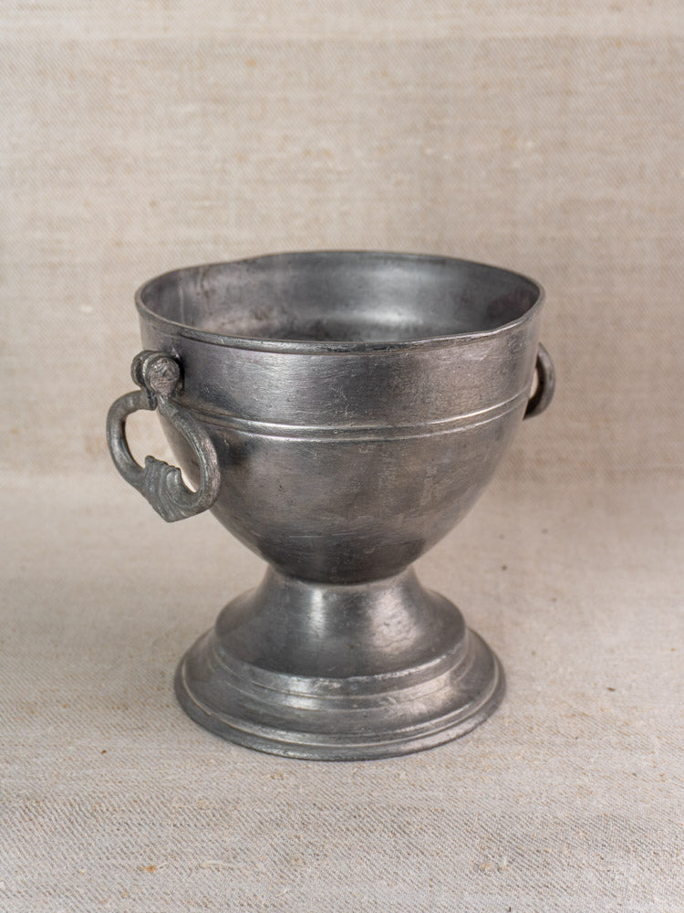 Mid 19th century French antique pewter footed bowl with ornate handles, on neutral fabric background.