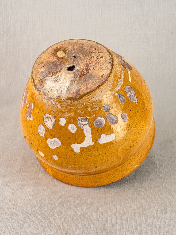 19th-century French yellow glazed terracotta pichet planter with white spots and worn base on neutral fabric background.