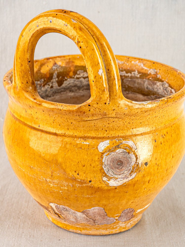 Antique French yellow-glazed terracotta pichet with curved handle and rustic wear, used as a hanging planter on fabric background.