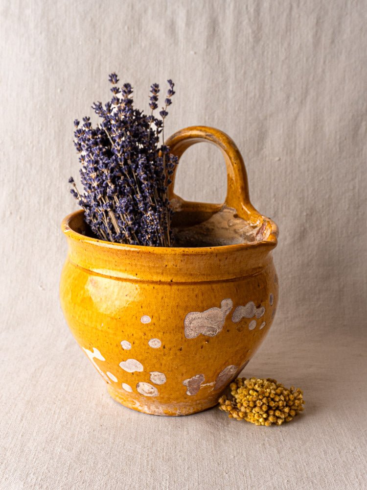 Antique French yellow glazed terracotta hanging planter with dried lavender and yellow flowers on neutral textured fabric.