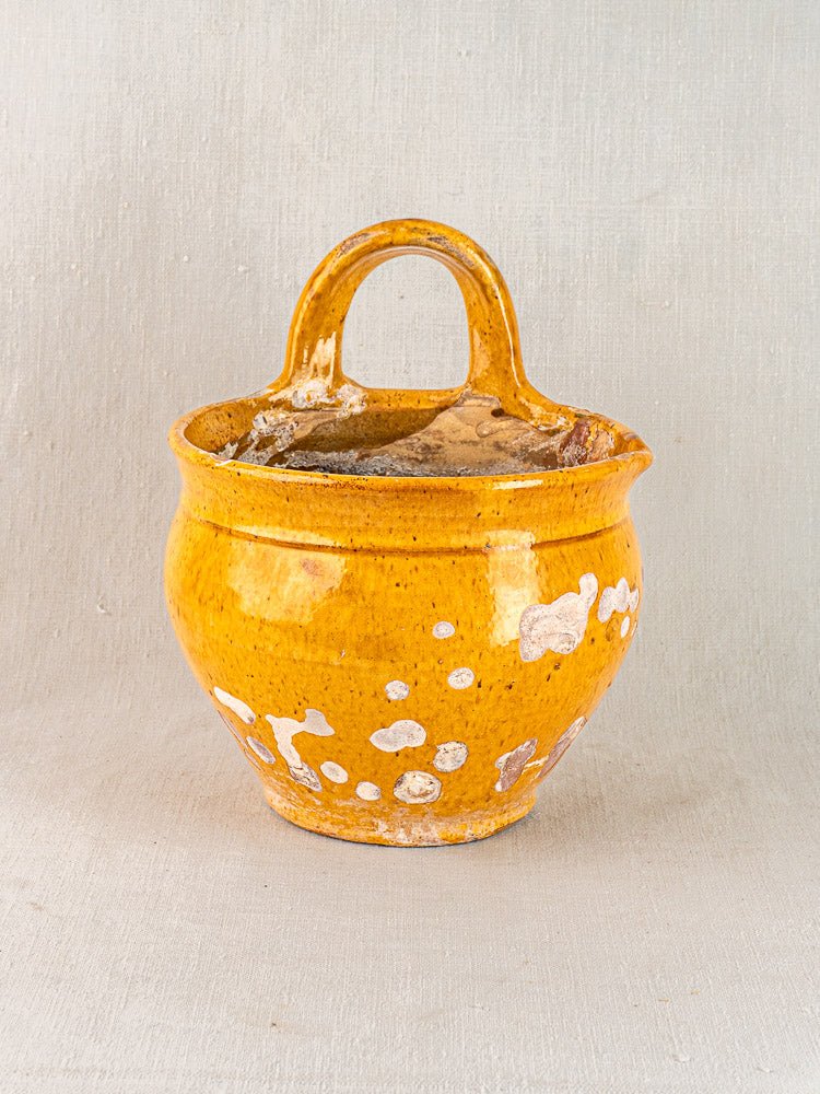 19th-century French yellow glazed terracotta hanging planter with rounded body, arched handle, and white wear marks on neutral background.