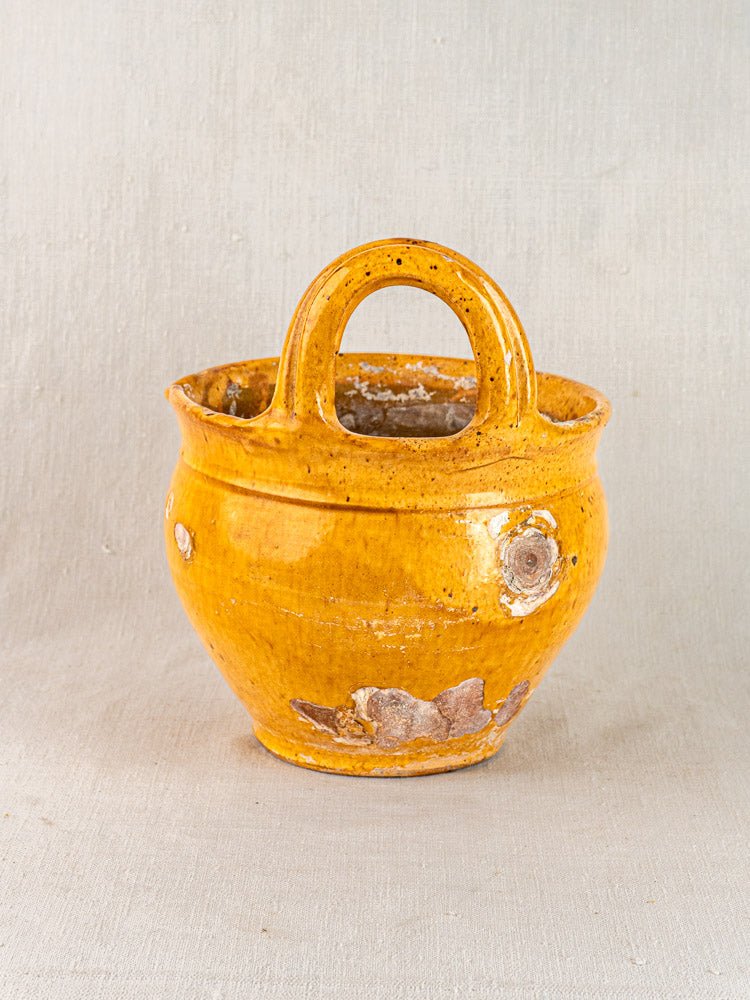 Antique French 19th-century yellow glazed terracotta hanging planter with wear and chipping on neutral fabric background.