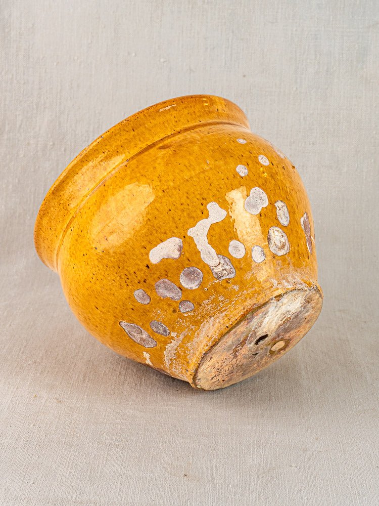 19th-century French yellow glazed terracotta pichet with white spots and rustic wear on a textured light gray background.