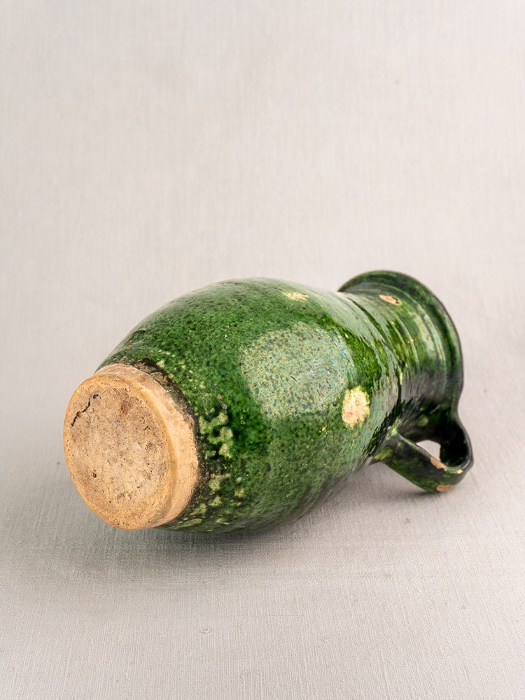 Antique French green glazed terracotta pitcher with rounded body and handle on light surface.