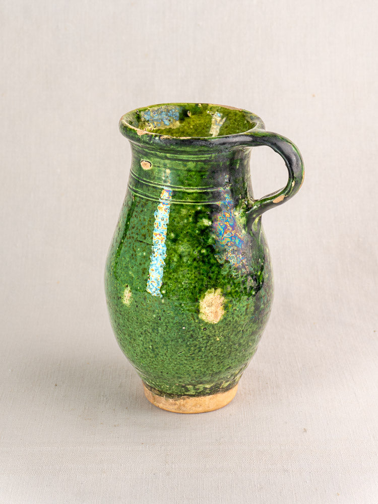19th-century French green glazed terracotta pitcher with handle, textured surface, and unglazed spots.