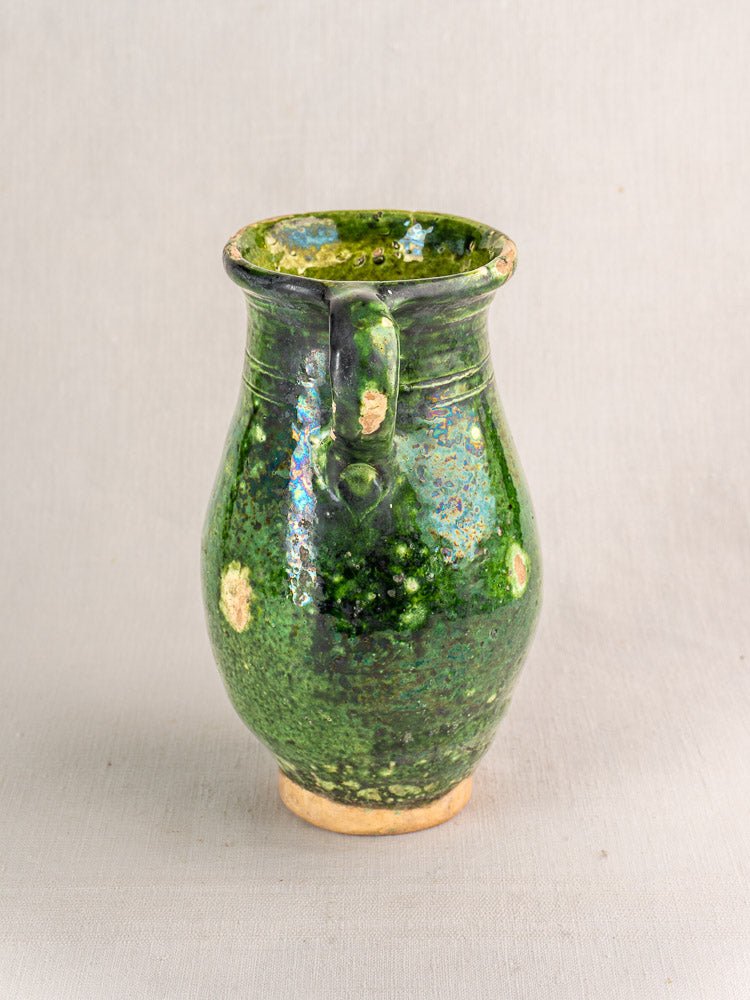 19th-century French green glazed terracotta pitcher with handle and exposed clay accents on plain background.