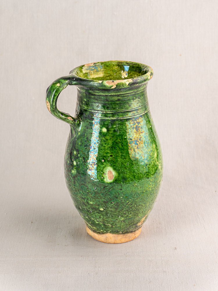 Antique French green-glazed terracotta pitcher with single handle, worn details, on light background.