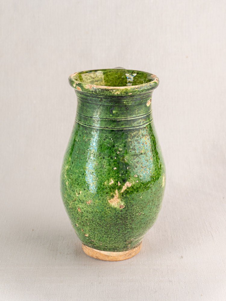 Antique French green glazed terracotta pitcher with wide body and subtle color variations on gray background.