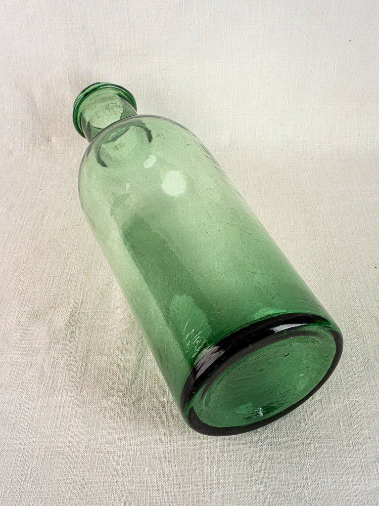 Antique French preserves bottle in green bubble glass, hand-blown and resting on a textured surface.