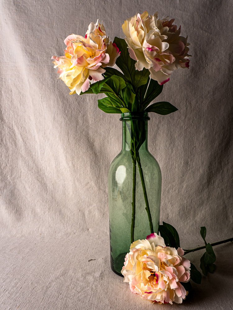 Antique French green bubble glass preserves bottle with pink and yellow flowers on beige cloth.