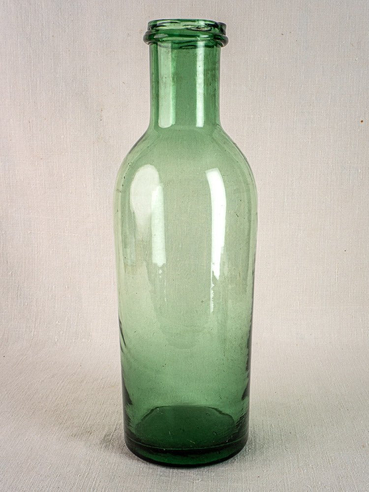 Antique French green bubble glass preserves bottle, hand-blown circa 1900, on textured surface.