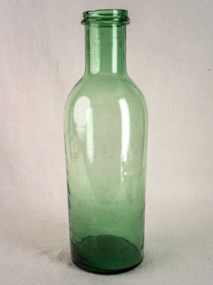 Antique French green bubble glass preserves bottle, hand-blown circa 1900, on a light textured surface.