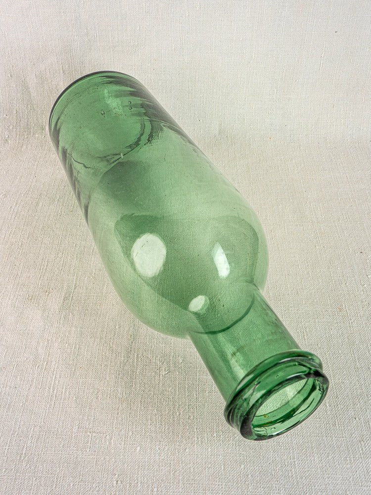 Antique French green bubble glass preserves bottle, hand-blown circa 1900, on textured fabric background.