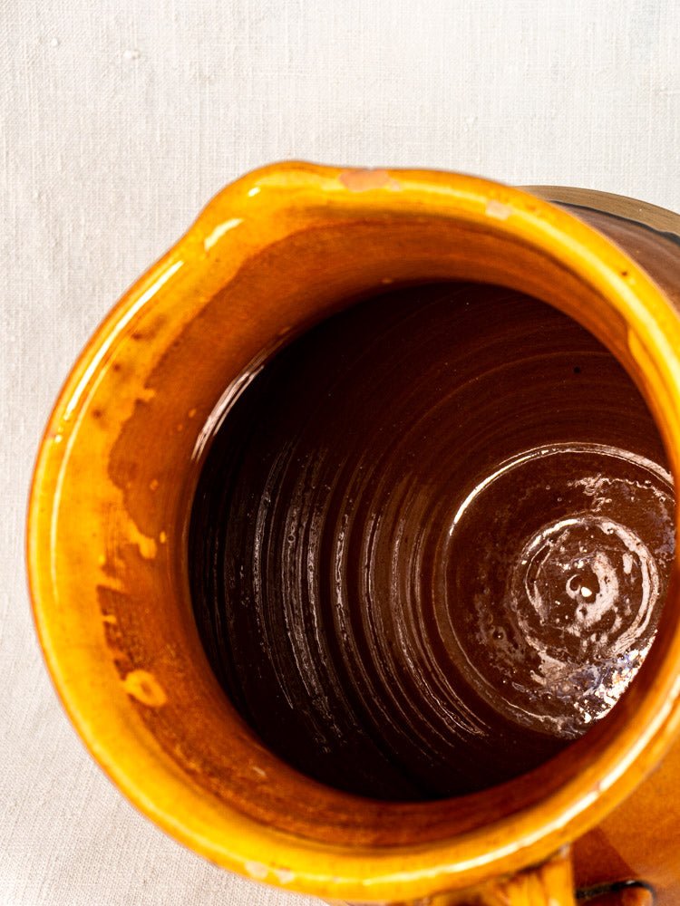 Vintage French Provençal pitcher in amber-glazed Aubagne terracotta, spiral interior, on light textured surface.