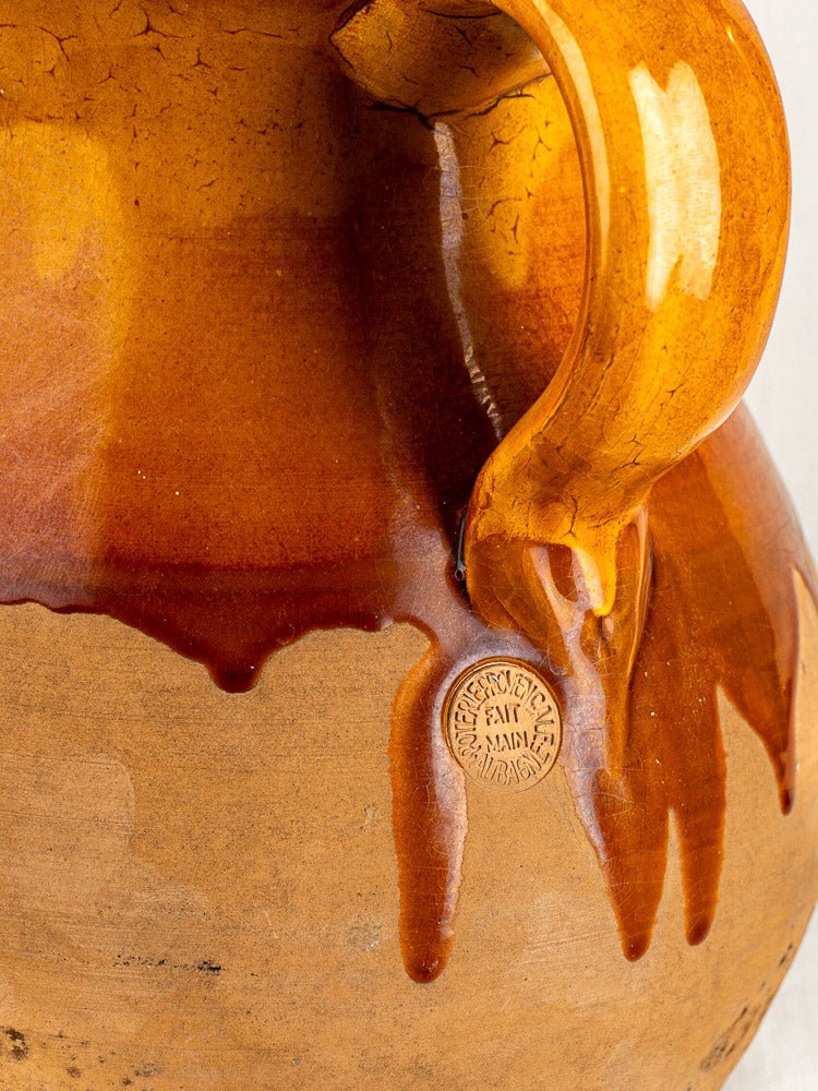 Vintage French Provençal terracotta pitcher in Aubagne, amber glaze drips over matte body, handle and maker’s stamp visible.
