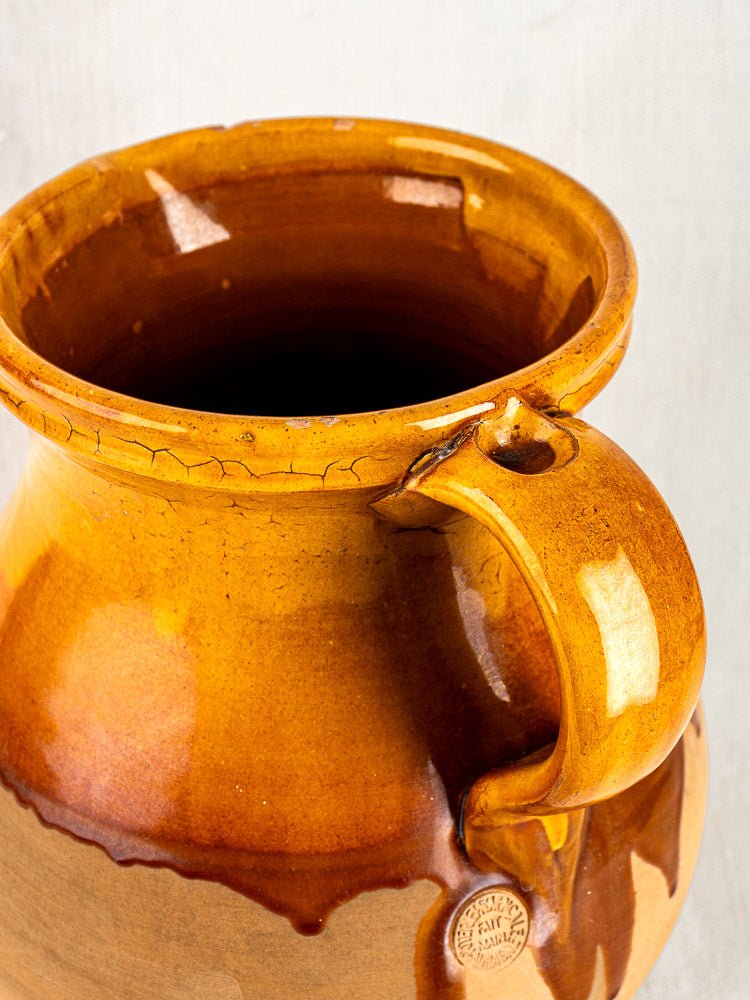 Vintage French Provençal terracotta pitcher with amber glaze, round body, large handle, and small rim cracks.