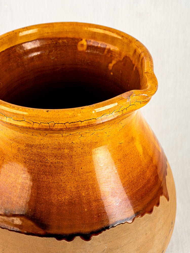 Vintage French Provençal pitcher in Aubagne terracotta with amber glaze and crackled rim, light background.