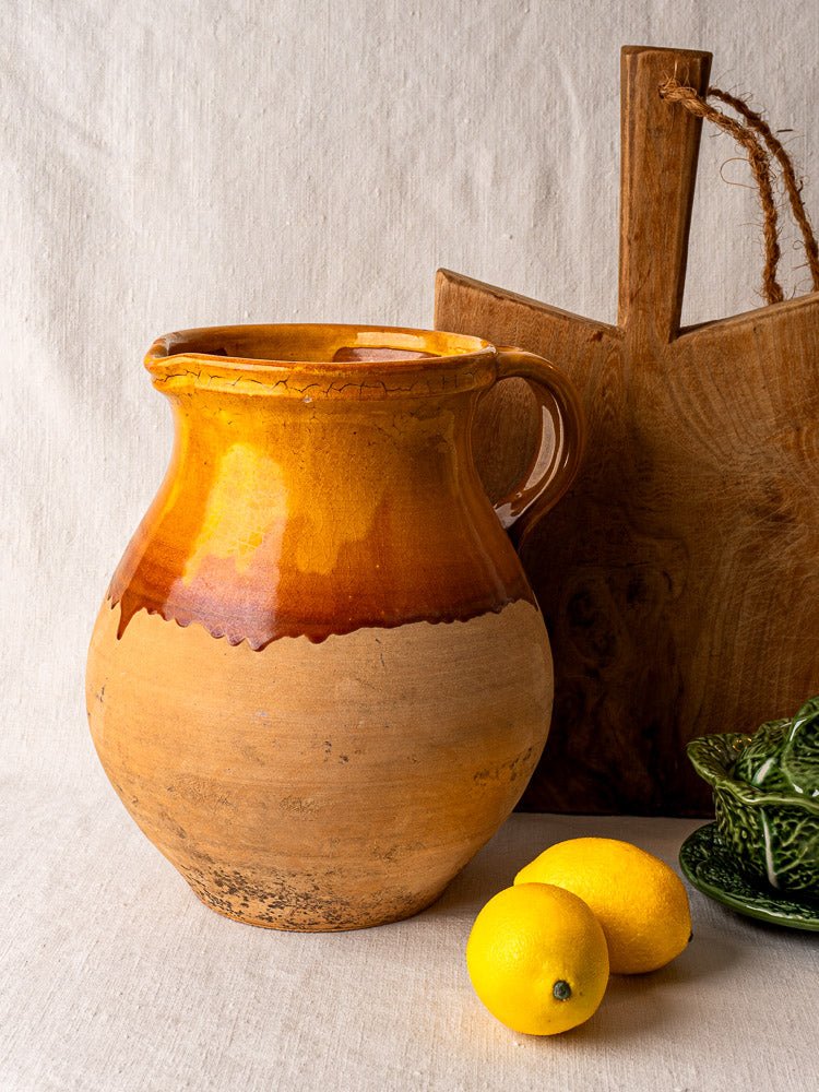 Vintage French Provençal Aubagne terracotta pitcher with amber glaze beside lemons and a wooden board.