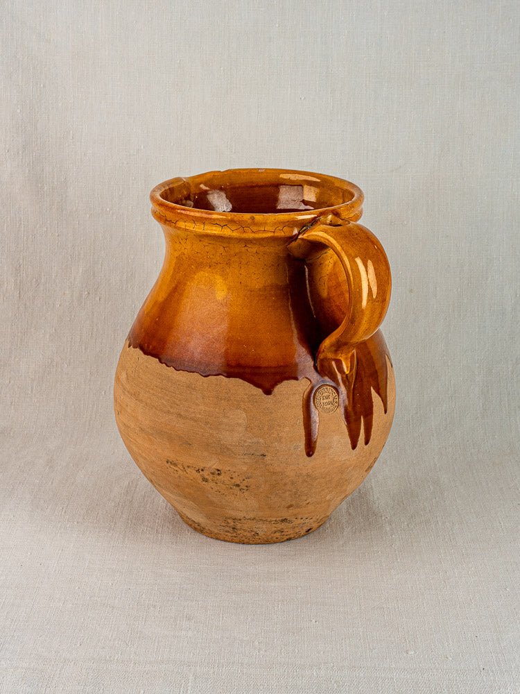 Vintage French Provençal Aubagne terracotta pitcher with amber glaze and matte lower section on fabric.