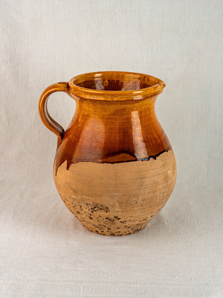 Vintage French Provençal Aubagne terracotta pitcher with single handle and glossy amber-glazed top on light fabric.