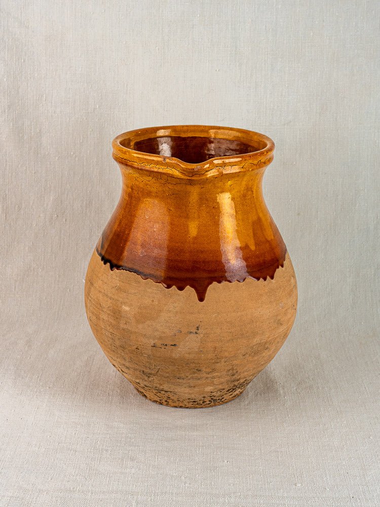 French Provençal terracotta pitcher with amber glazed top and matte lower half, on light fabric.
